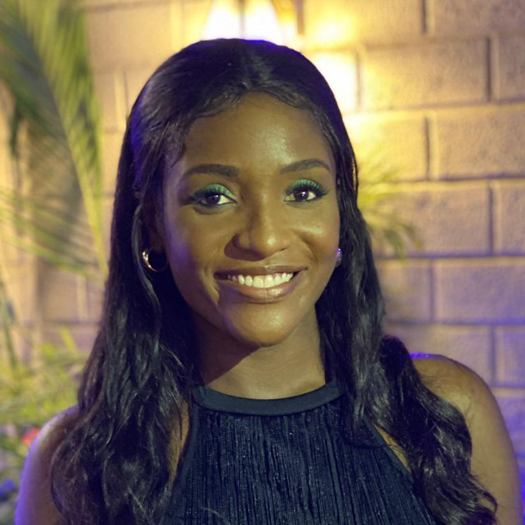 A young black lady with long hair smiles at the camer