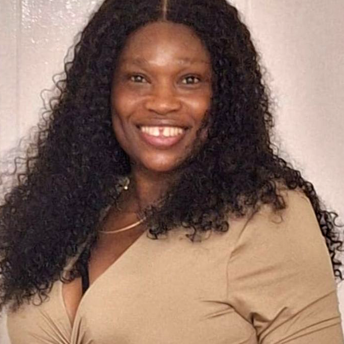 A black woman with long hair, wearing a beige blouse, smiling at the camera