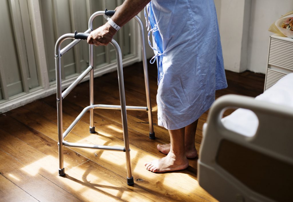 A woman standing and holding on the a walking frame. Only the lower half of her body is visible